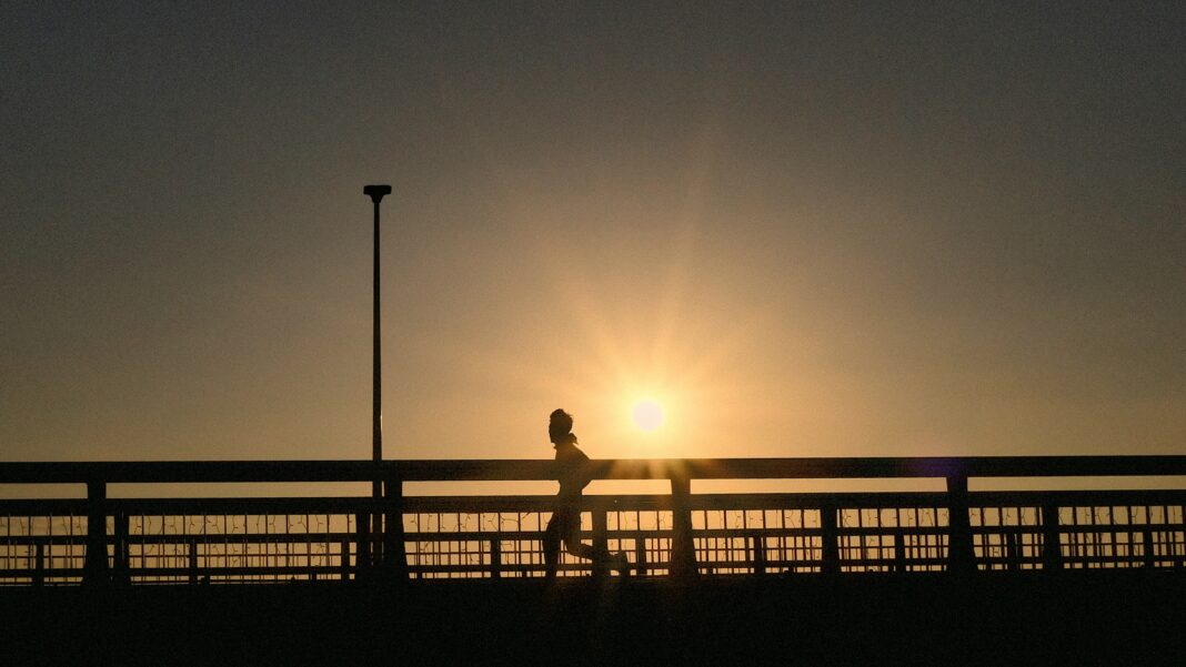 Runner wearing light, moisture-wicking clothing jogging on a sunny trail during summer, staying hydrated in hot weather conditions.