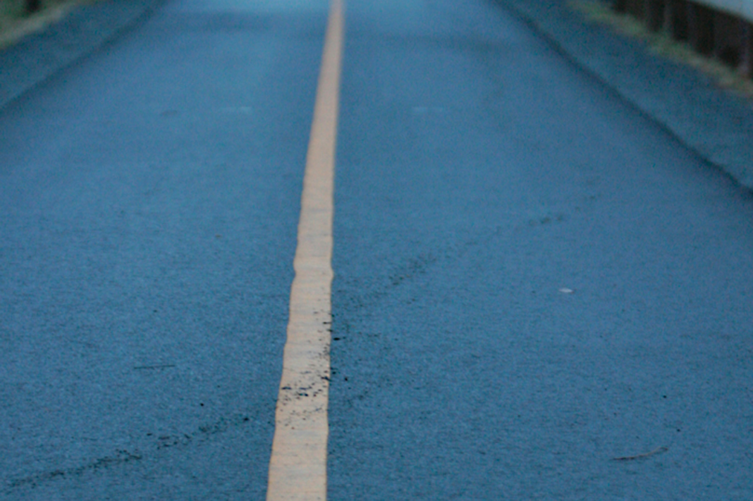 Single yellow centerline on an empty blue-tinted road, symbolizing pacing and direction for marathon long runs