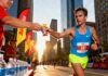 Marathon Fueling Guide 2025: 7 Smart Nutrition Rules Every Runner Can Actually Follow Marathon runner grabs an energy gel at a city race aid station, hydration tables and crowd in background