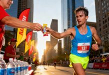 Marathon Fueling Guide 2025: 7 Smart Nutrition Rules Every Runner Can Actually Follow Marathon runner grabs an energy gel at a city race aid station, hydration tables and crowd in background