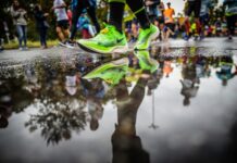 Couch to 10K: A Realistic Plan for Your First 10K Neon green running shoes mid-stride beside a puddle reflecting runners at a 10K road race