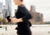 How Much Does an Online Running Coach Cost? Runner moving through a city skyline while checking her phone, representing online running coaching