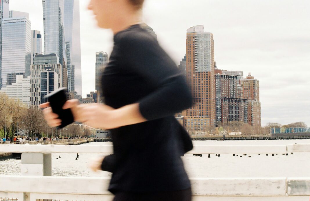 Runner in the city checking her phone Runner moving through a city skyline while checking her phone, representing online running coaching
